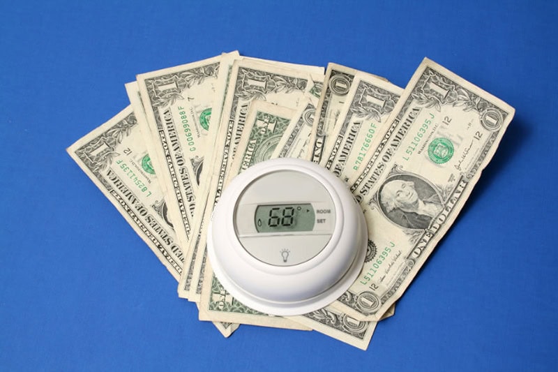 Thermostat sitting on dollar bills on a blue background.