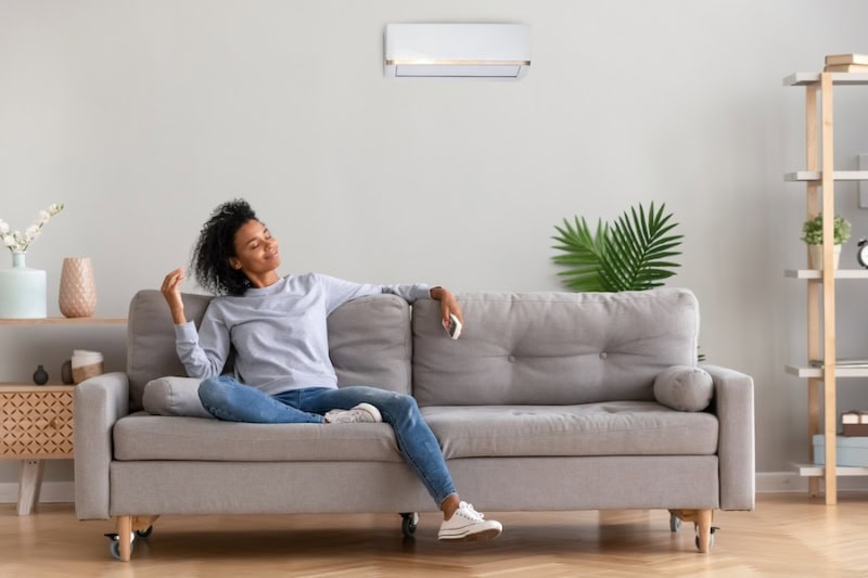 Ductless Mini Splits for Comfortable and Healthy Living. African young relaxed woman sitting on couch breathing fresh air.
