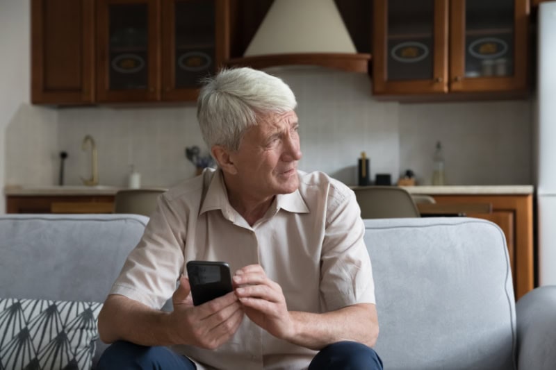 What’s That Smell Coming From My Furnace? Photo of a man sitting on his couch, seemingly concerned with his phone in his hand.