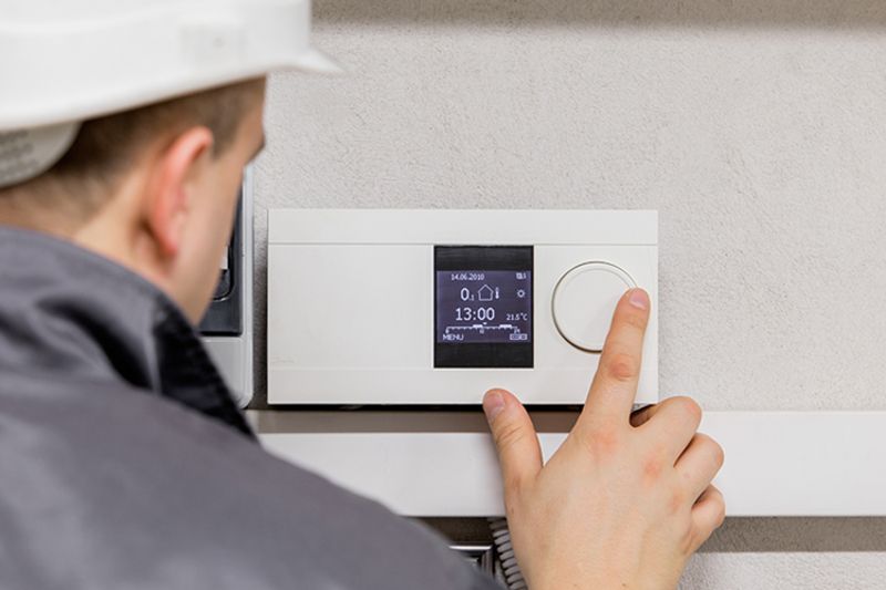 Image of technician fiddling with thermostat. Why Schedule Air Conditioning Maintenance?