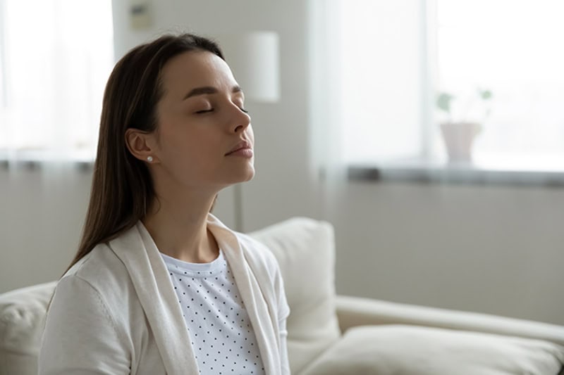 Woman sitting on couch, breathing in clean air.