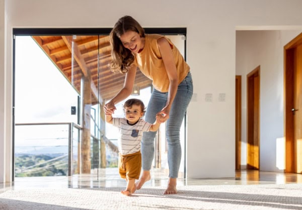 Toddler learning how to walk at home with the help of his mother.